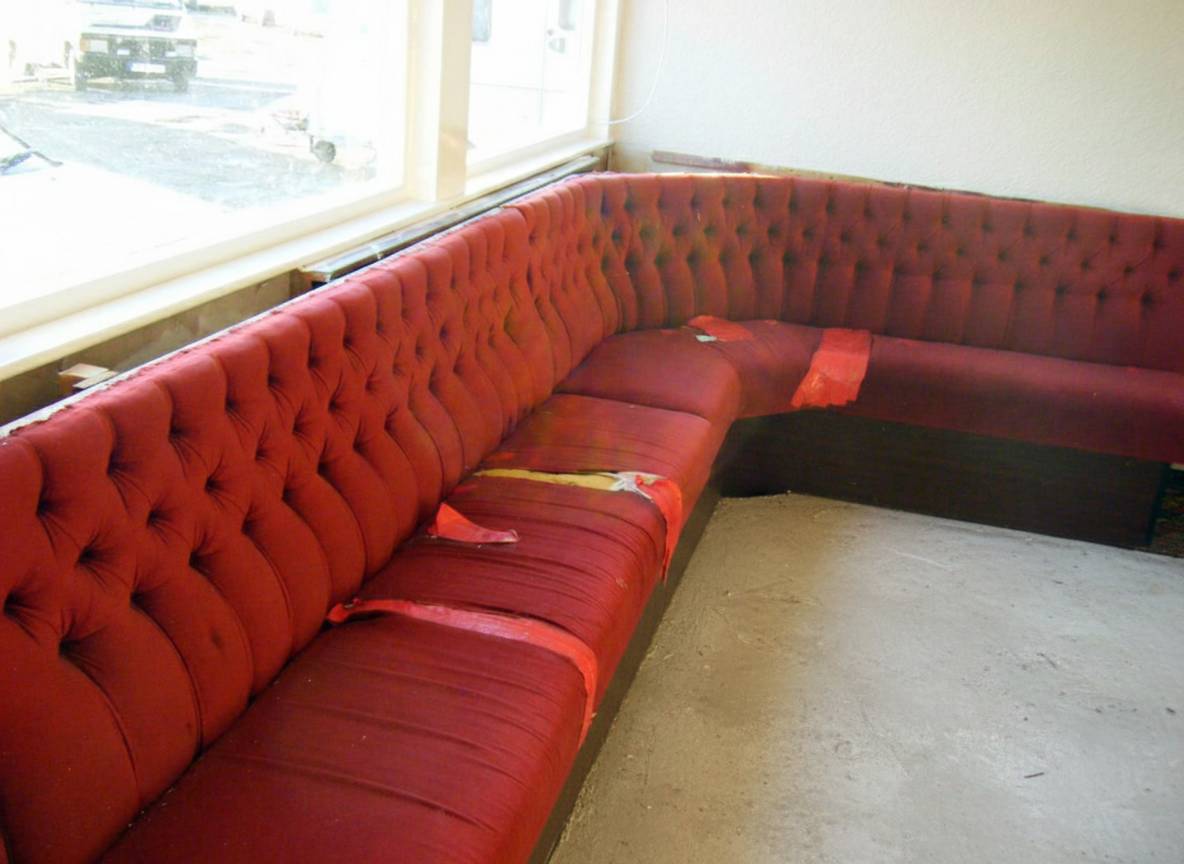 Worn L-shaped club bench in torn red vinyl